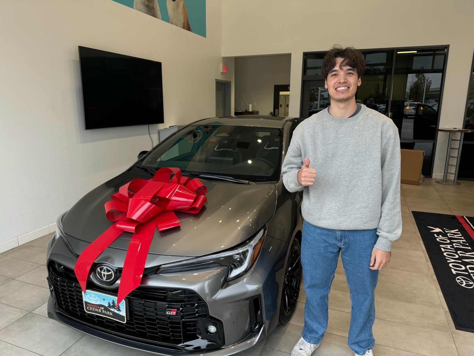Smiling with a thumbs-up next to my new GR Corolla with a red bow at Toyota of Cedar Park