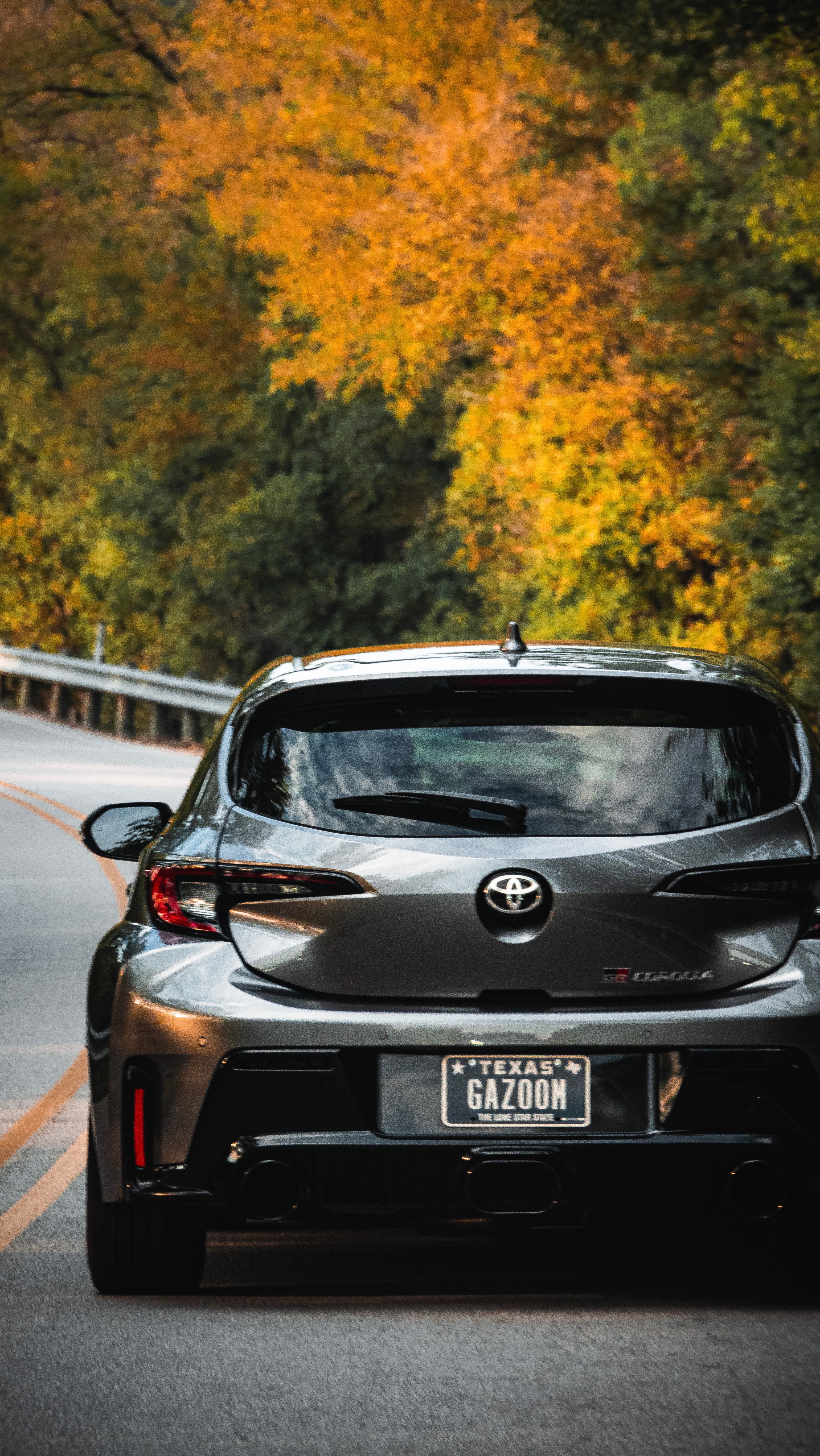 Rear view of the GR Corolla on a winding road lined with fall foliage